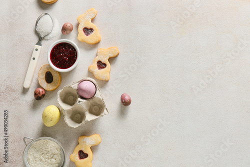 Tasty Easter cookies, painted eggs and bowl with jam on light background
