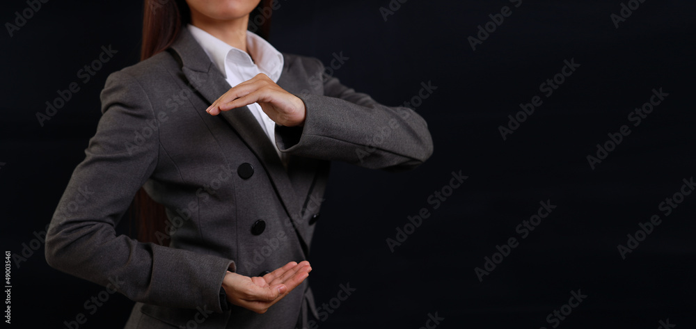 Attractive professional female hands in classic suit show protecting something. Businesswoman standing with black background. Property insurance and security concept