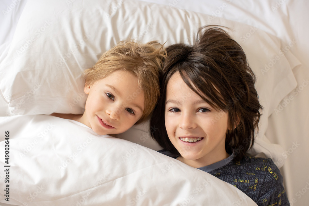 Two children, blond toddler boy and older brother, cuddling in bed in the morning, love and tenderness Two children, blond toddler boy and older brother, cuddling in bed in the morning, love and tenderness