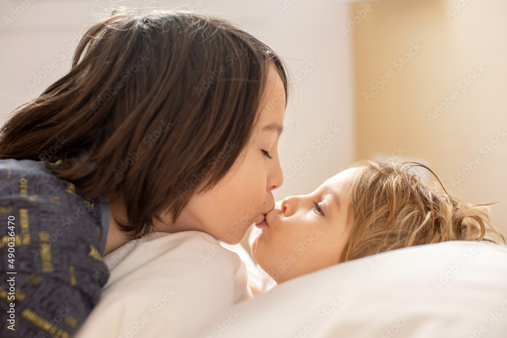 Two children, blond toddler boy and older brother, cuddling in bed in the morning, love and tenderness