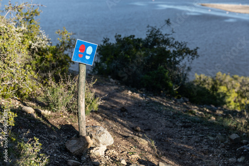 Ein blauer Wegweiser für den Wanderweg im De Hoop Natuere Reserve in Südafrika, welcher durch das grüne Landschaftsidyll mit Büschen, Bäumen und Seenlandschaft führt photo