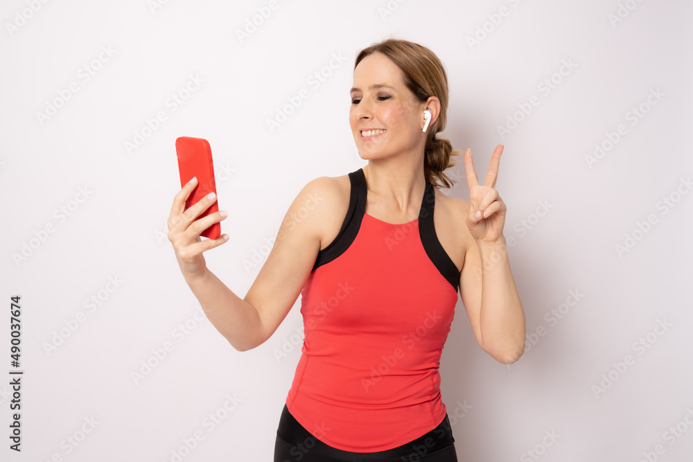 Happy young woman in sports clothing smiling and holding smart phone and listen music on white background. Happy young woman in sports clothing smiling and holding smart phone and listen music on white background.