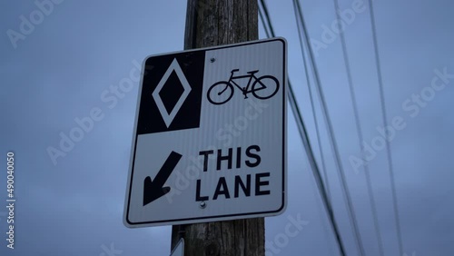 HOV bike lane diamond sign on wooden post in urban area with exposed telephone wires and electricity lines - sign for bikers, cyclists, and bicyclists - road rules and signs for bicycles on cloudy day photo