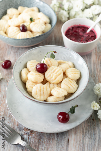 Traditional Ukrainian lazy cottage cheese dumplings served with sour cream and cherry sauce and fresh cherries on a wooden background.