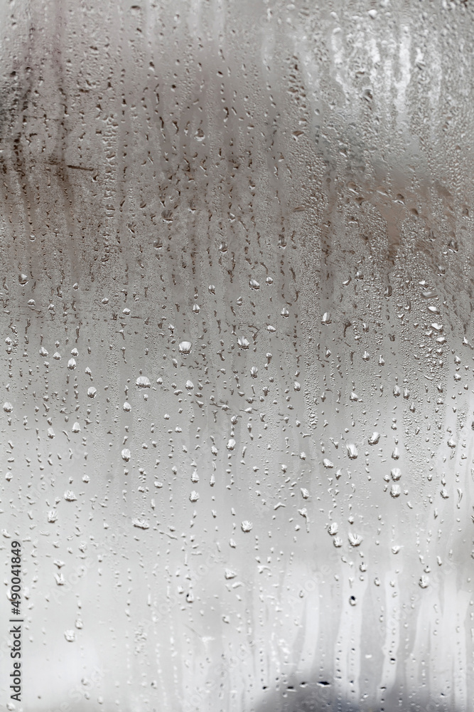 Fototapeta premium Condensation on glass with drops flowing down, Vertical natural background, humidity and foggy blank. Outside , bad weather, rain