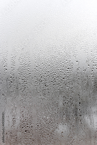 Vertical natural background, condensation on glass with drops flowing down, humidity and foggy blank. Outside , bad weather, rain