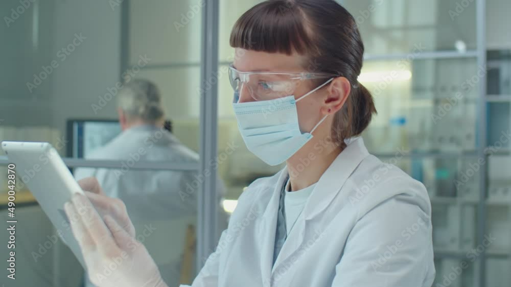 Female scientist in protective mask, gloves and glasses working on digital tablet in laboratory Female scientist in protective mask, gloves and glasses working on digital tablet in laboratory