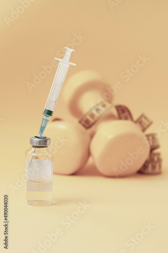 syringe is stuck in jar, dumbbells and measuring tape on yellow background are lying next to it, a vertical photo. concept of doping in sports, steroids, testosterone and other drugs for weight loss.