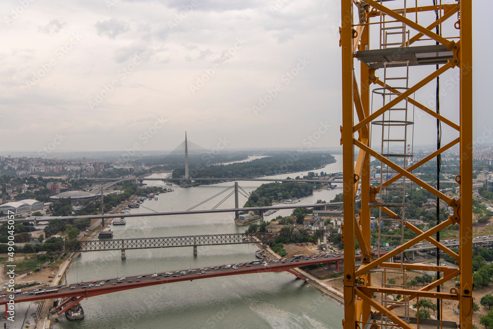 Closeup view of yellow Crane Access Ladder, steel staircase. Construction site of high-rise structure, skyscraper. Beautiful scenic river, bridges and city view in background.