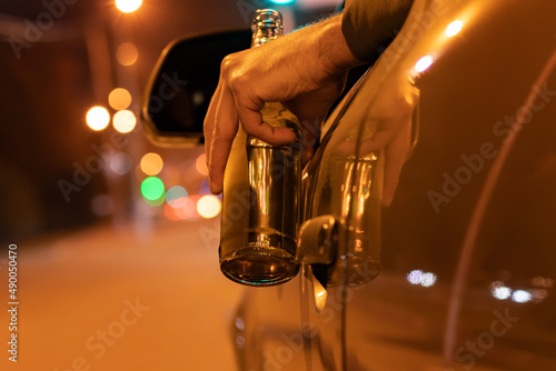 Drunk man driving a car with a bottle of beer at the night. Don't drink and drive concept photo