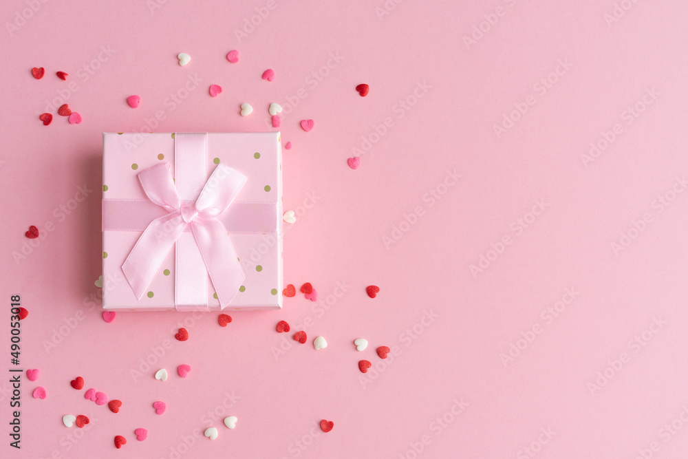 Gift box with ribbon bow and topins decoration on pink background. Copy space.