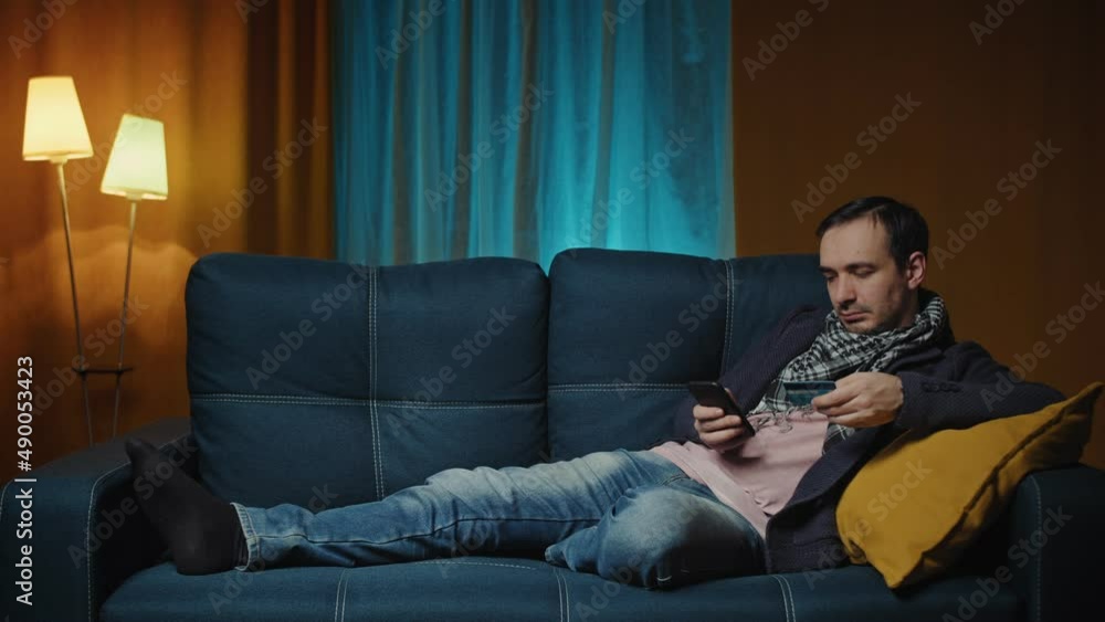 Man lies on a cozy sofa and makes payment online by credit card. Online payment service. Man lies on a cozy sofa and makes payment online by credit card. Online payment service.