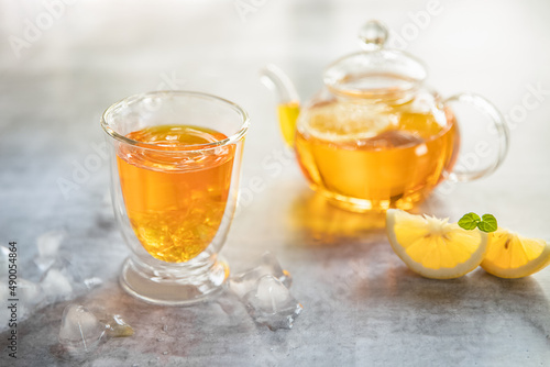 iced lemon fruit tea in a glass cup and tea pot isolated over plain grey background, no people. food summer refreshment concept