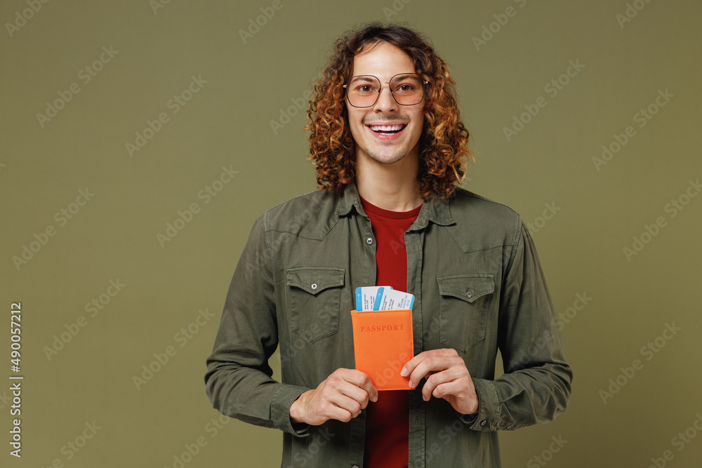 Traveler tourist smiling excited fancy stunning fun young brunet curly man 20s wears khaki shirt jacket glasses hold passport boarding tickets isolated on plain olive green background studio portrait. Traveler tourist smiling excited fancy stunning fun young brunet curly man 20s wears khaki shirt jacket glasses hold passport boarding tickets isolated on plain olive green background studio portrait.