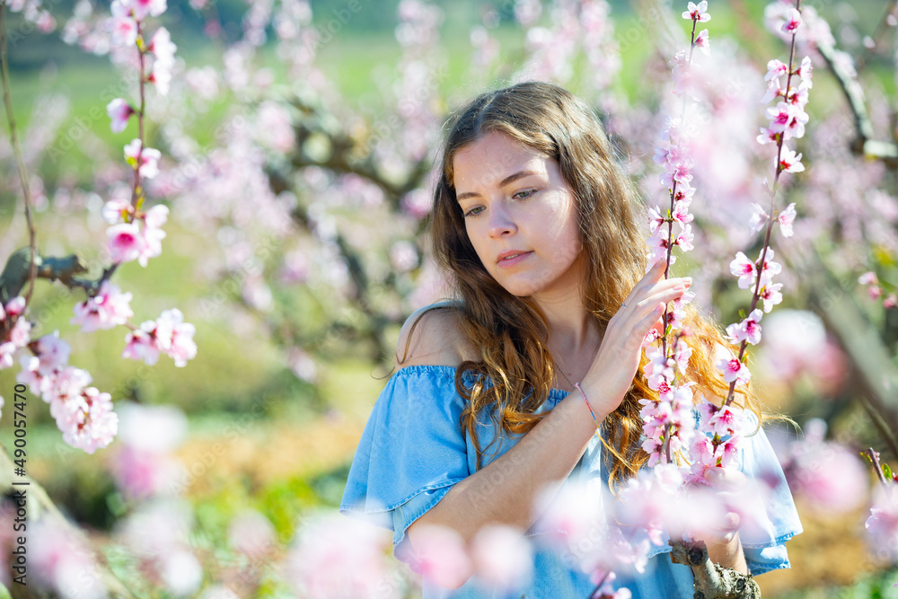 Portrait of pretty young woman standing next to blossoming peach tree at sunny spring day