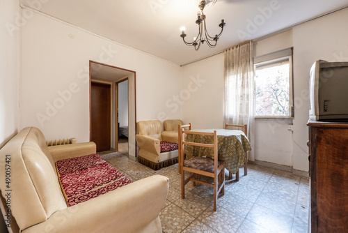 Vintage living room with couch in the center and sofas with cushions upholstered in hideous fabric and terrazzo floors