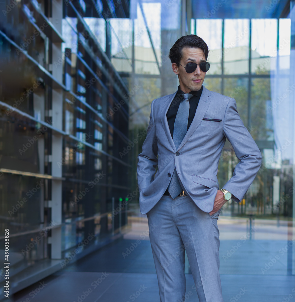 three quarter lenght shot of a handsome man in formal suit with a rogue expression in his shaved face while standing with hands in pockets in an entry of an offices building three quarter lenght shot of a handsome man in formal suit with a rogue expression in his shaved face while standing with hands in pockets in an entry of an offices building