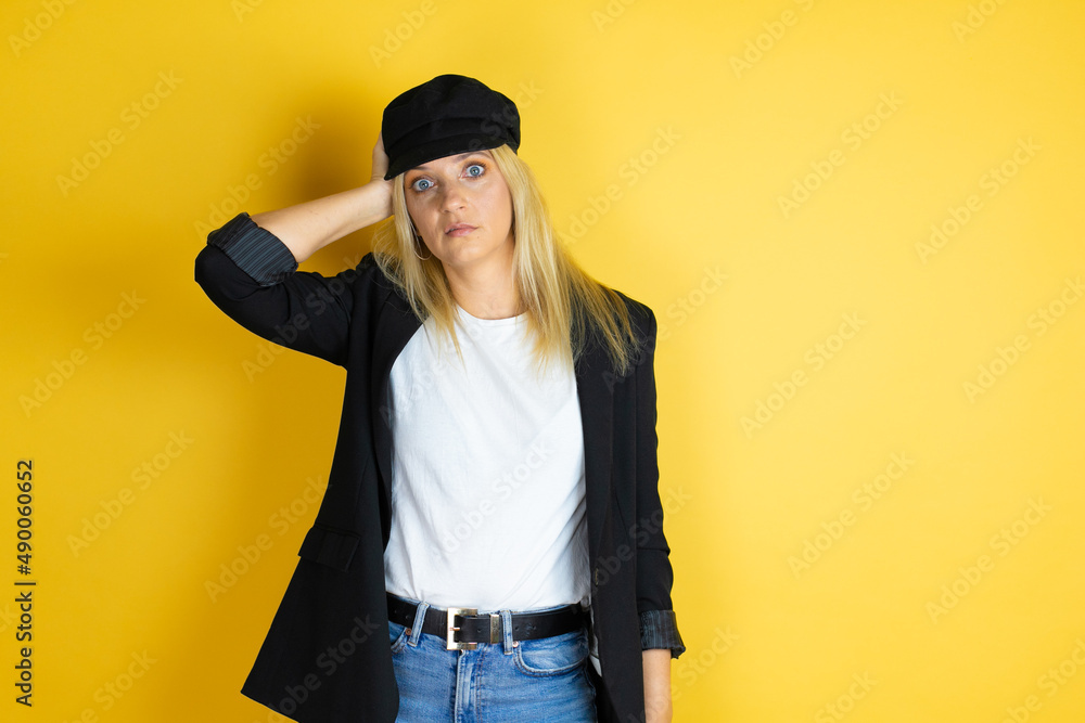 Beautiful woman wearing casual white t-shirt and a cap over isolated yellow background putting one hand on her head smiling like she had forgotten something