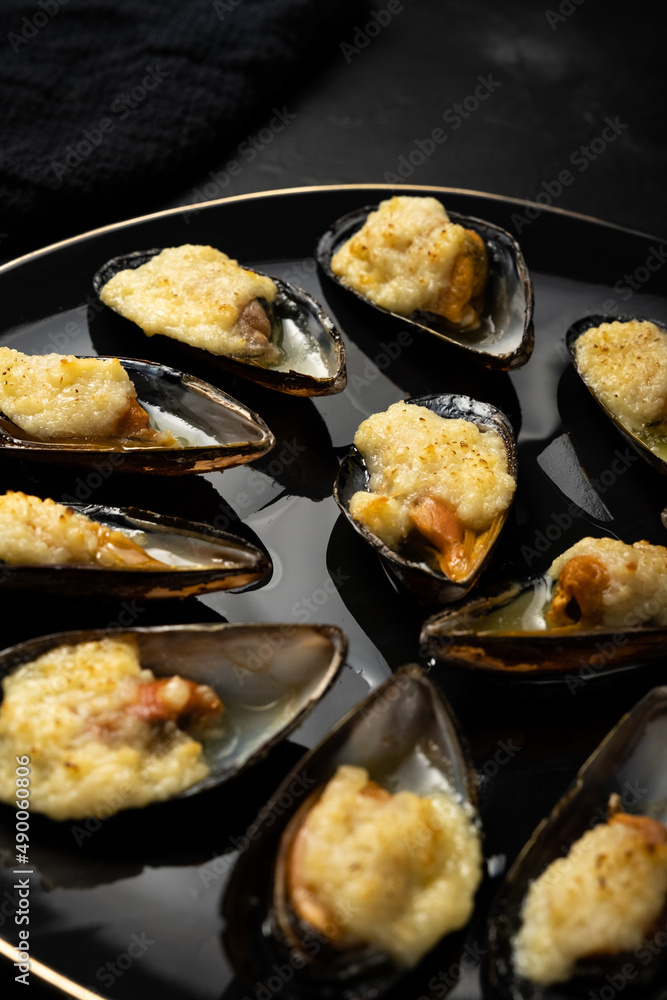 baked mussels in shells with creamy sauce poured with oil on a black plate on a dark background baked mussels in shells with creamy sauce poured with oil on a black plate on a dark background