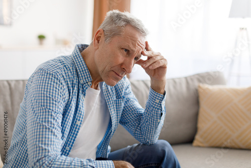 Stressed mature man sitting on couch and thinking