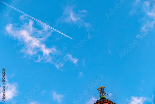 airplane in the blue sky with white clouds over the rooftop of a building