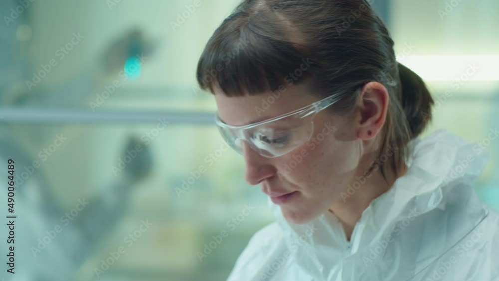 Young female doctor in protective glasses putting on face mask, then pulling hood of coverall suit over her head, zipping it and walking away Young female doctor in protective glasses putting on face mask, then pulling hood of coverall suit over her head, zipping it and walking away