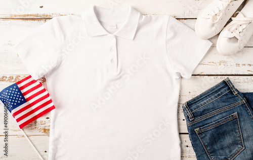 Mockup design white polo t shirt for logo, top view on white wooden background with US flag, shoes and jeans