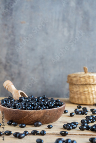 Top view of small black beans on table with bowl and basket, selective focus, gray background, vertical