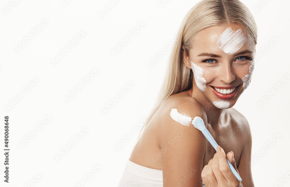 Vertical shot of beautiful blond girl applying facial mask, standing in towel after shower with clean hydrated skin, using brush for lotion, face scrub, white background Vertical shot of beautiful blond girl applying facial mask, standing in towel after shower with clean hydrated skin, using brush for lotion, face scrub, white background
