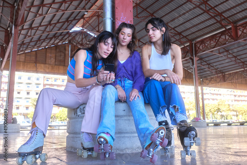 Friends using the mobile while sitting on an urban area wearing classic skates
