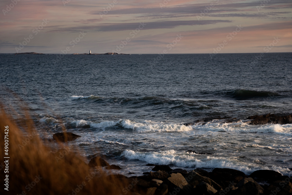 Outdoor coastal sunset view over ocean waves from rocky shore of Sachuest Point in Middletown Rhode Island with Sakonnet Lighthouse in the distance