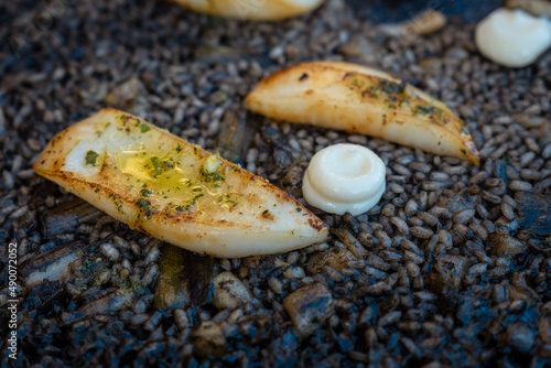 Detail of the black rice with cuttlefish and young garlic with aioli, a plate of dry rice, cooked in paella or in a clay pot, a characteristic flavor of Valencian Mediterranean cuisine. Spain