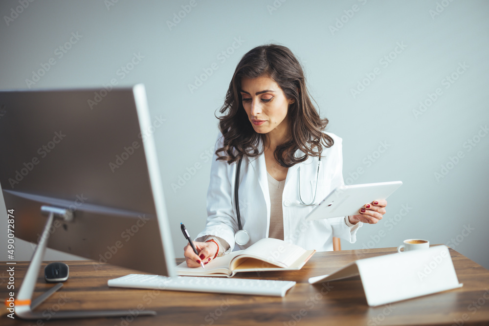 Portrait Of Smiling Female Doctor Wearing White Coat With Stethoscope In Hospital Office. Smiling doctor holding a tablet PC in a modern office. Portrait Of Smiling Female Doctor Wearing White Coat With Stethoscope In Hospital Office. Smiling doctor holding a tablet PC in a modern office.