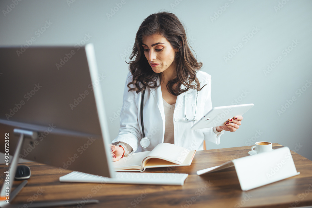 Portrait Of Smiling Female Doctor Wearing White Coat With Stethoscope In Hospital Office. Smiling doctor holding a tablet PC in a modern office. Portrait Of Smiling Female Doctor Wearing White Coat With Stethoscope In Hospital Office. Smiling doctor holding a tablet PC in a modern office.