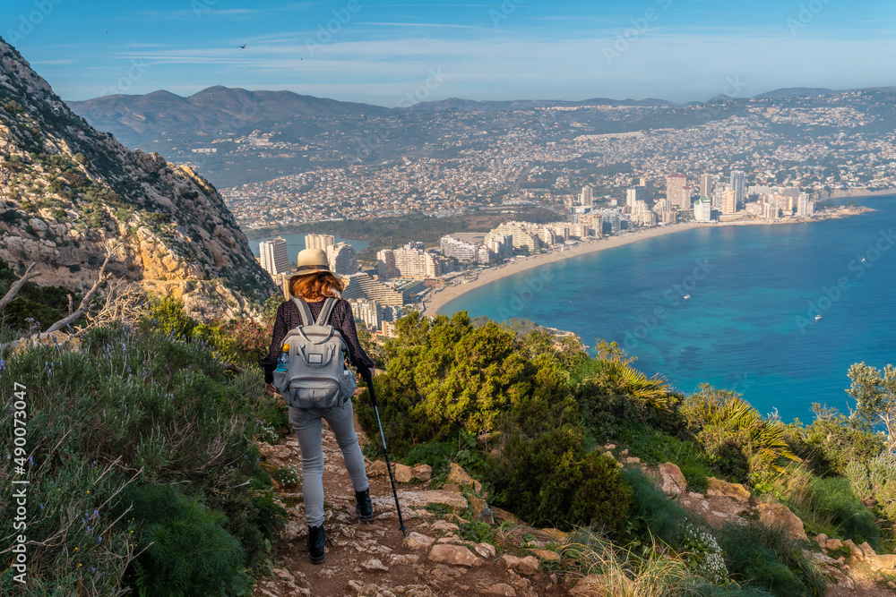 A young woman descending from the top of the Penon de Ifach Natural Park with the city of Calpe in the background, Valencia. Spain. Mediterranean sea. View of La Fossa beach