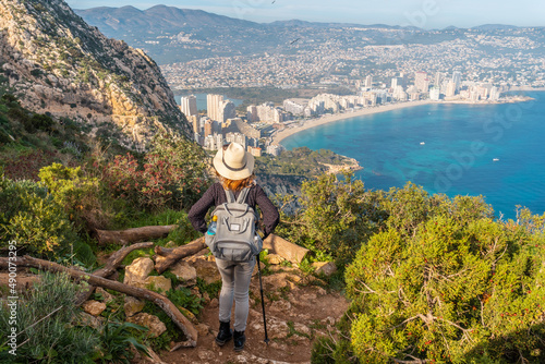 A young hiker on the descent path of the Penon de Ifach Natural Park with the city of Calpe in the background, Valencia. Spain. Mediterranean sea. View of La Fossa beach
