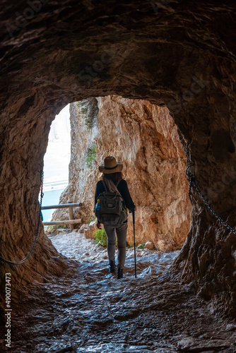 A young hiker in the tunnel of the trail in the Penon de Ifach Natural Park with the city of Calpe in the background, Valencia. Spain. Mediterranean sea. View of La Fossa beach