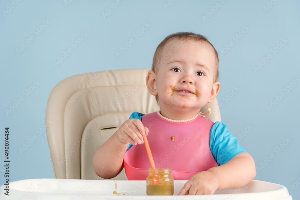 Toddler eats broccoli vegetable puree with an orange plastic spoon while sitting on a feeding chair Toddler eats broccoli vegetable puree with an orange plastic spoon while sitting on a feeding chair