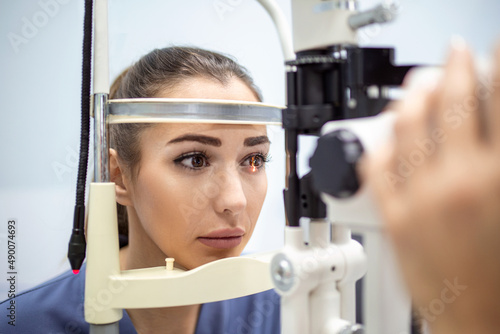 Attentive optometrist examining female patient on slit lamp in ophthalmology clinic. Young beautiful woman is diagnosed with eye pressure on special ophthalmological equipment.