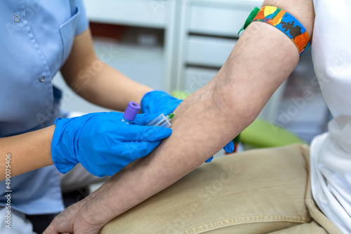 Preparation for blood test with pretty young woman by female doctor medical uniform on the table in white bright room. Nurse pierces the patient's arm vein with needle blank tube.