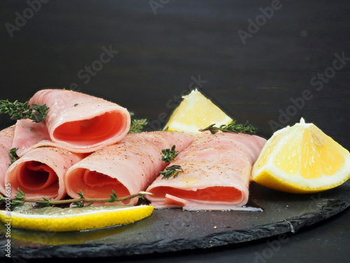 Thin slices of cooked ham served with olive oil, thyme, rosemary, spices and lemon slices. Close-up
