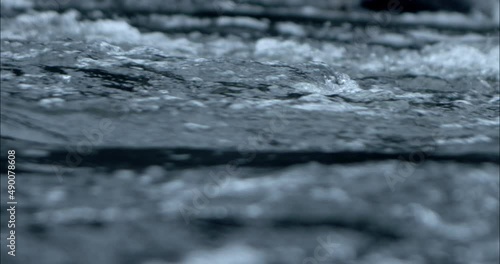 Close-up of water flowing by in slow motion on a river from the side with depth of field,