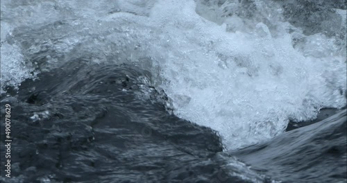 Close-up camera shot of water in slow motion on a river with a wave-like current.