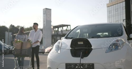 Multi ethnic couple charge elctric car after shopping photo