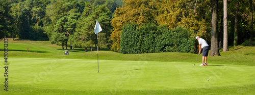 Golfer on the green with a putter in his hands. A player on the green evaluates the slopes and distance from the hole before aiming the ball towards the flag. photo