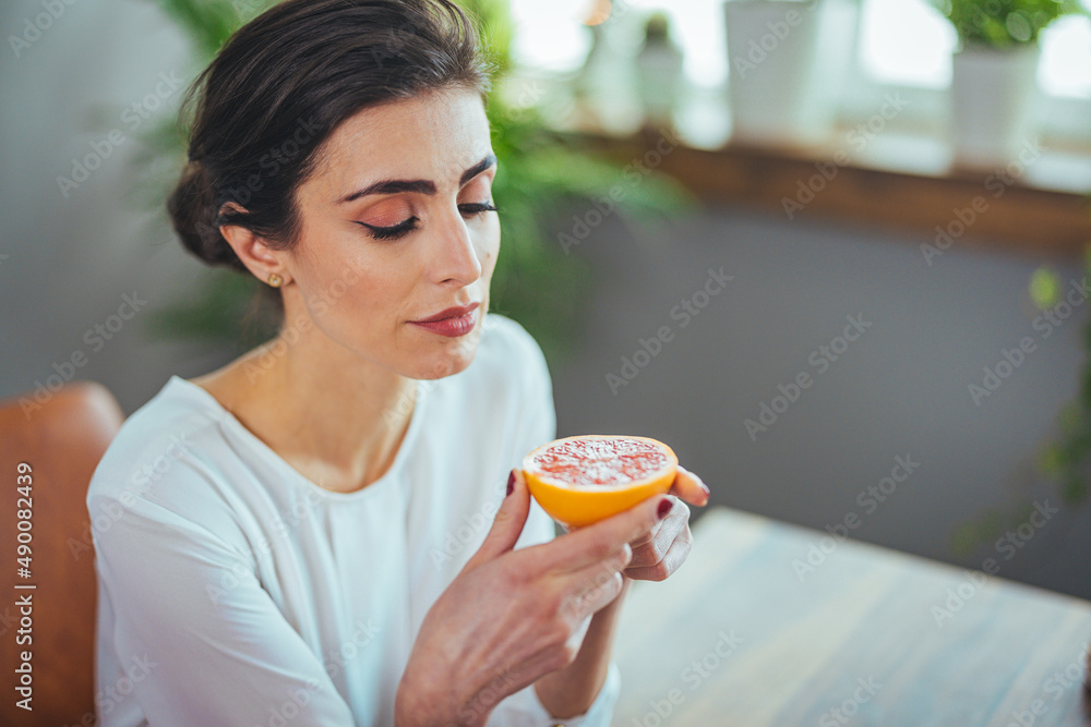 Woman with half a grapefruit. Portrait of a young girl with closed eyes enjoying the aroma of fresh, juicy grapefruit. Sick woman trying to sense smell