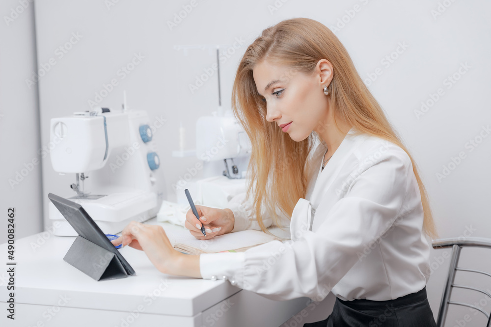 Concept online tailor, young woman talking through tablet and writing down measurements for dress or suit