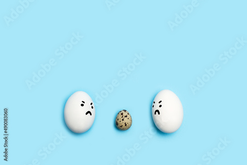 Un huevo de codorniz y huevos de gallina blancos alrededor sobre un fondo celeste liso y aislado. Vista superior. Copy space, Concepto: Discriminación, Acoso photo