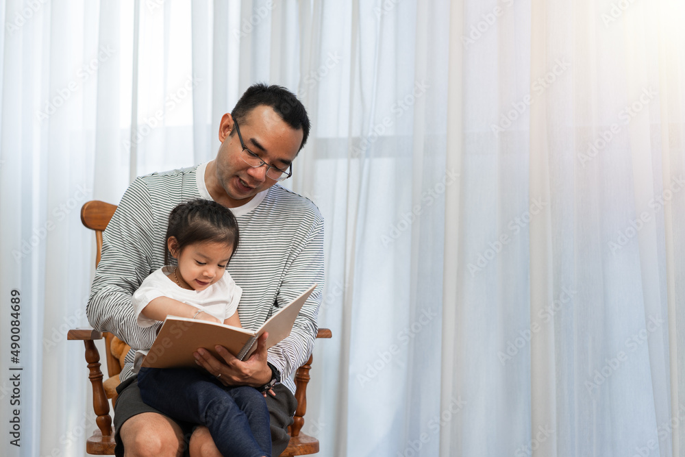 Asian father reading storybook to daughter in living room, family concept and early childhood development Asian father reading storybook to daughter in living room, family concept and early childhood development