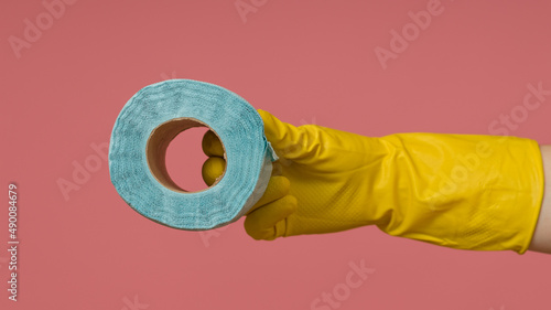 a hand in a yellow rubber glove holds a roll of toilet paper on a colored background